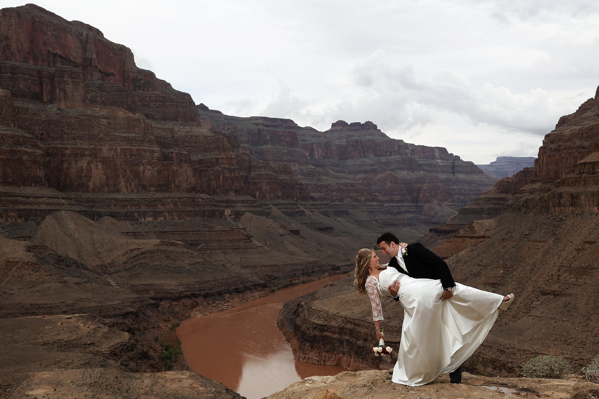 A bride and groom kissing on a cliff overlooking the grand canyon.