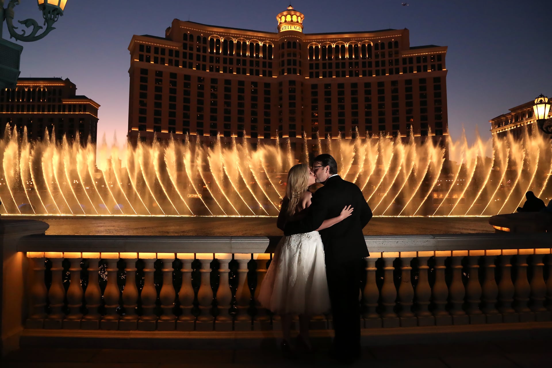 A bride and groom kiss in front of a fountain in las vegas.