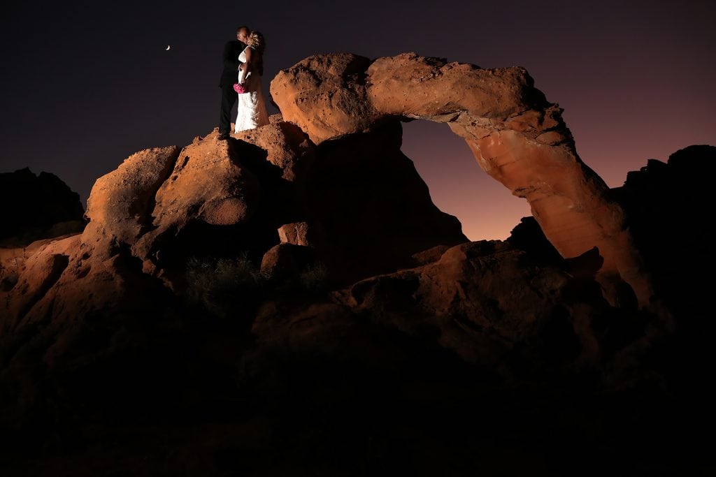 A bride and groom standing on a rock formation at night.