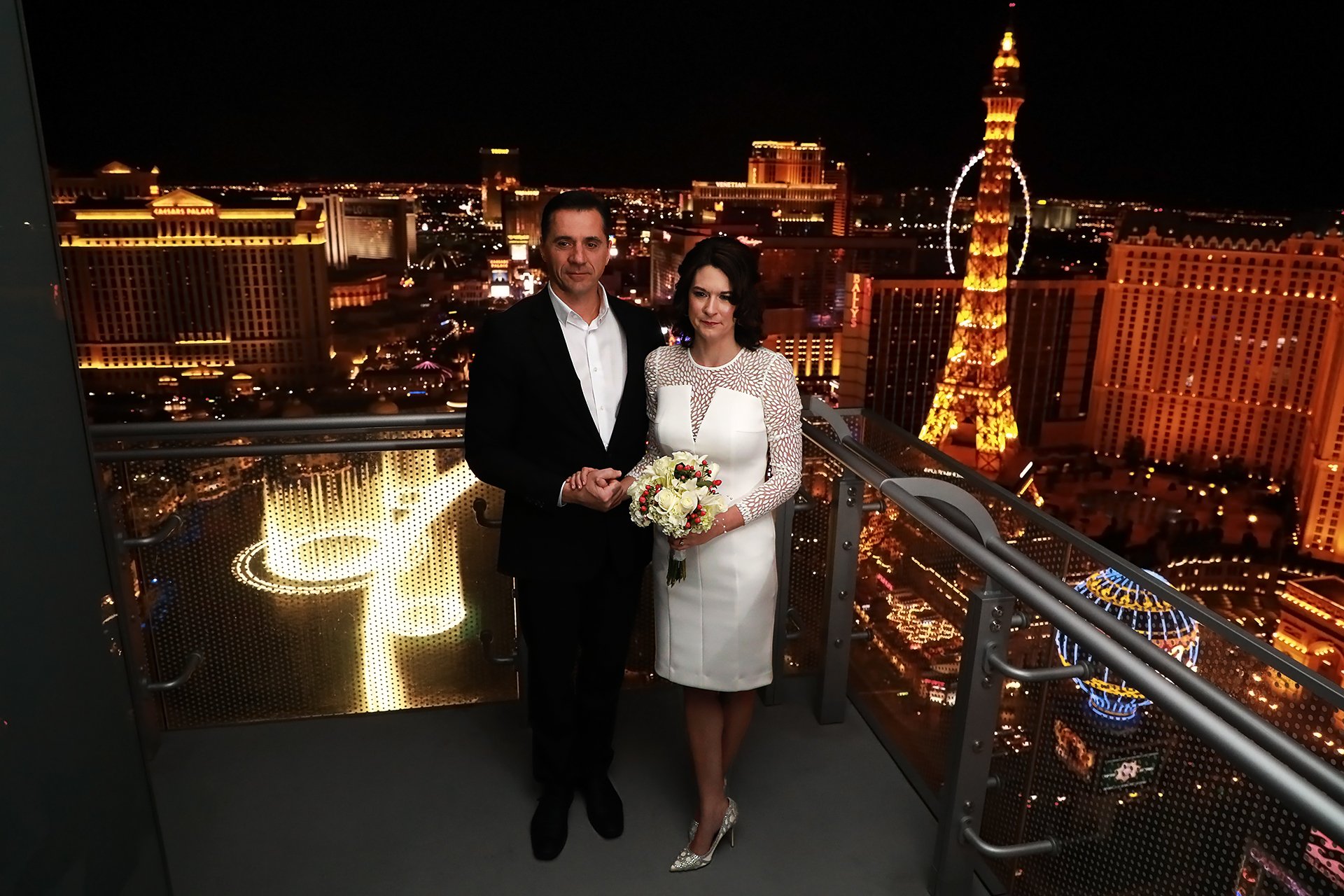 A bride and groom standing on a balcony overlooking the las vegas strip.