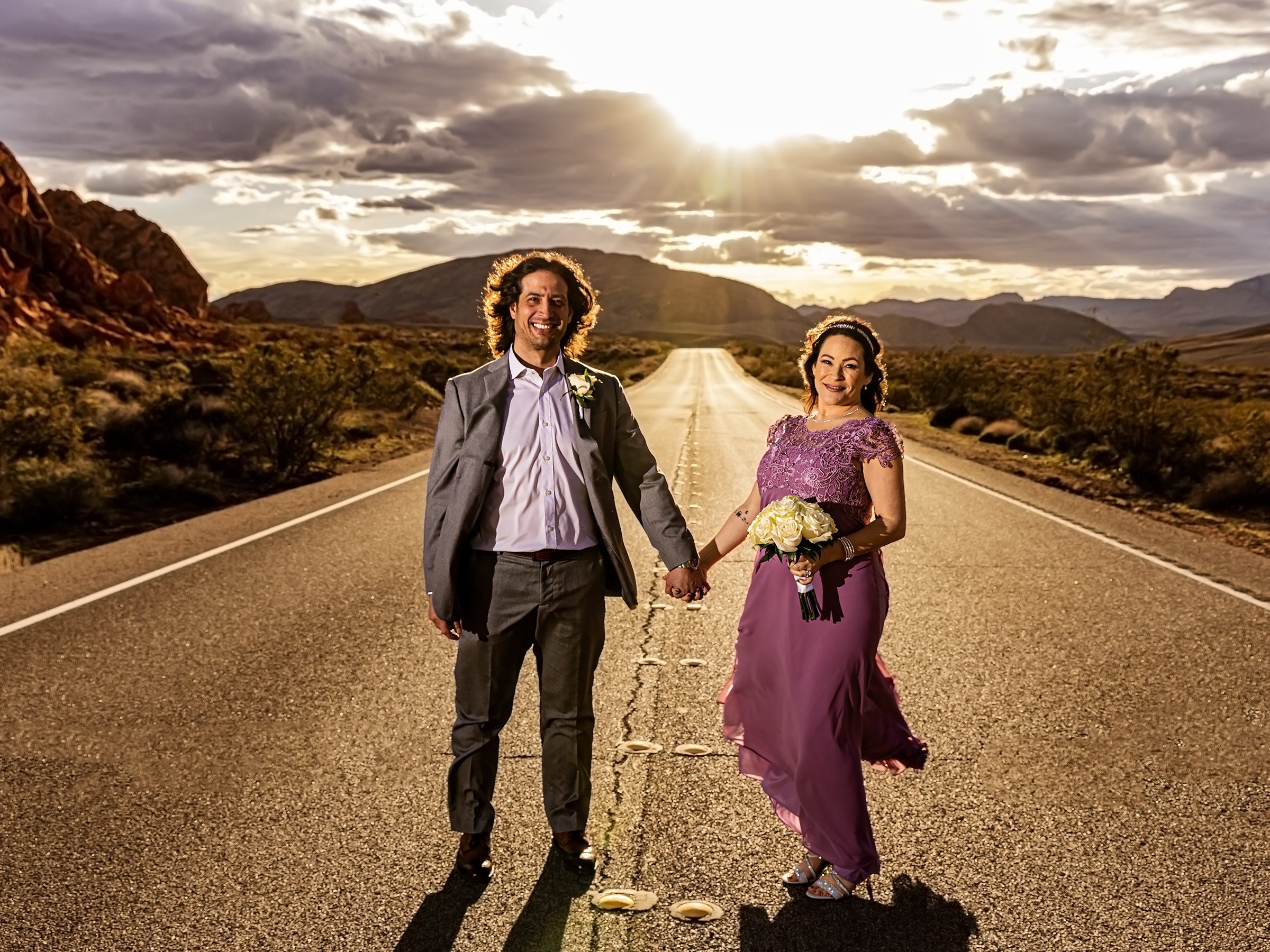 A couple elopes, holding hands on a desert road in the Valley of Fire.
