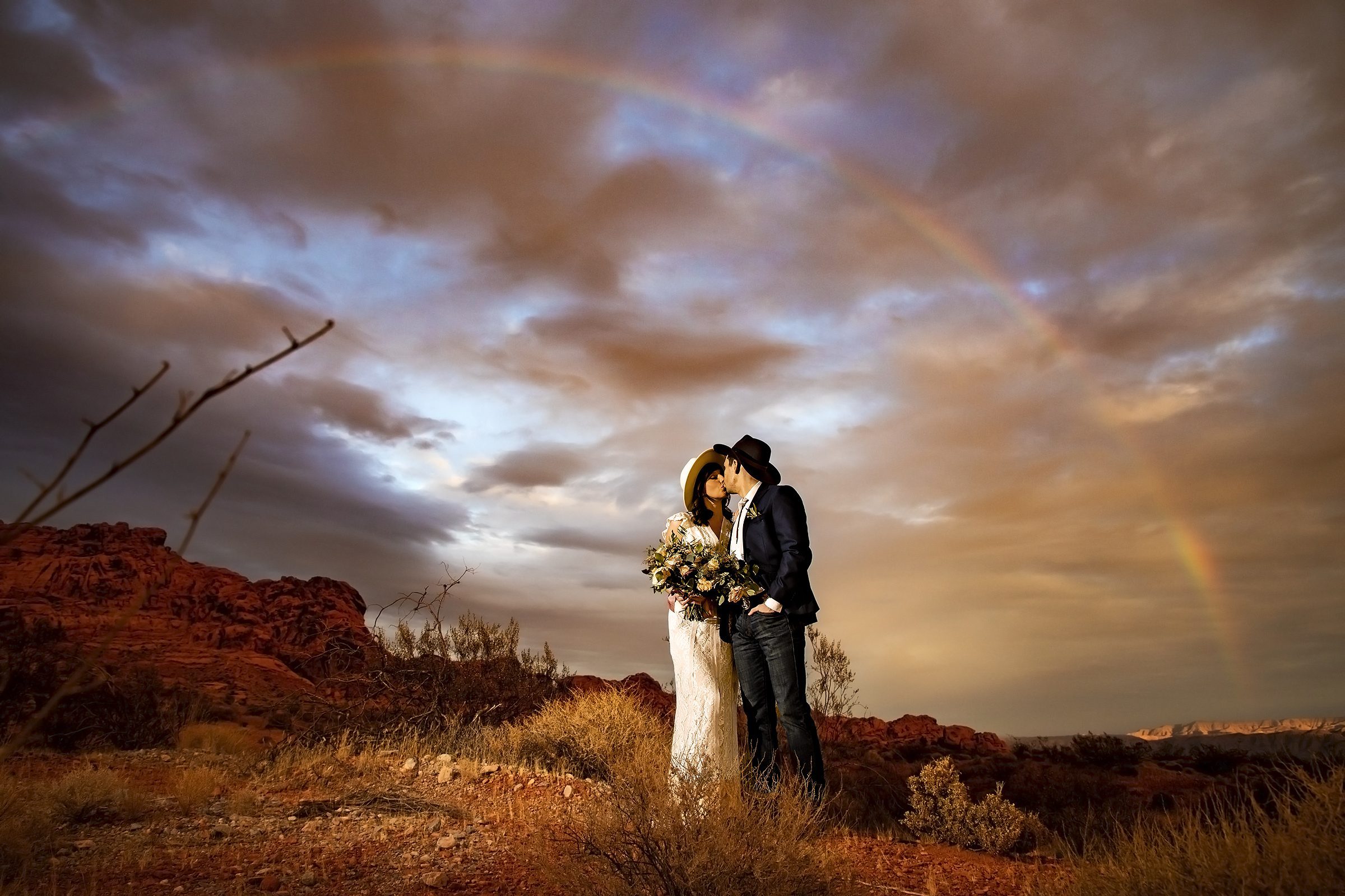 A bride and groom kiss in front of a rainbow during their Valley of Fire wedding.